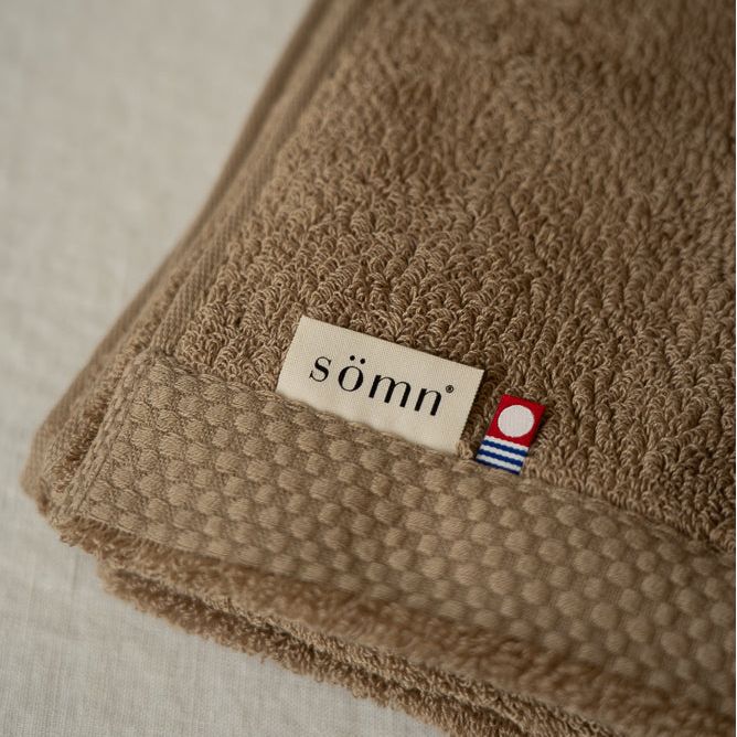Brown textured towel with 'sömn' label on a light background
