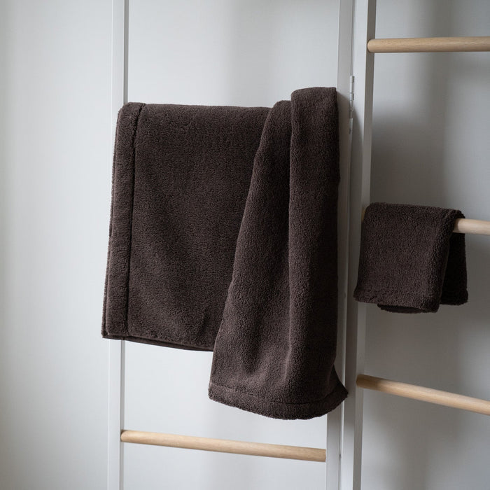 Brown towel hanging on a wooden rack against a white wall.