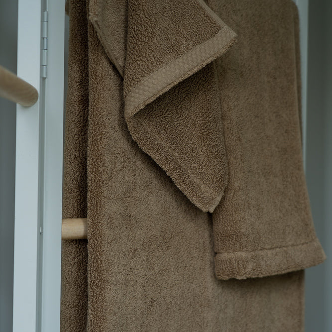 Brown towel hanging on a wooden rack against a neutral background