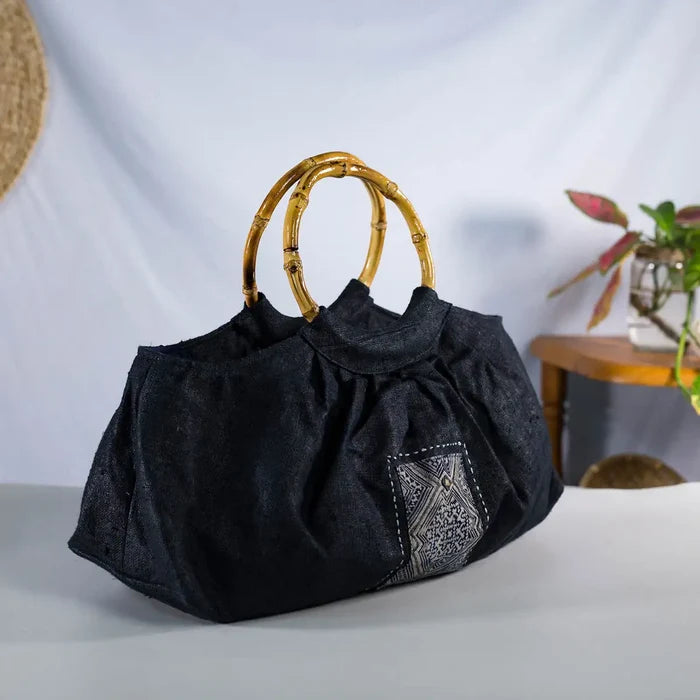 Black hemp handbag with bamboo handle, angled side view showing H’Mong patch, Purity Collection.