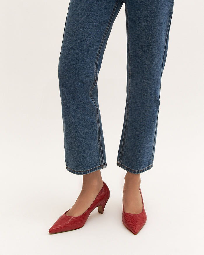 Blue jeans worn with red high-heeled shoes on a white background