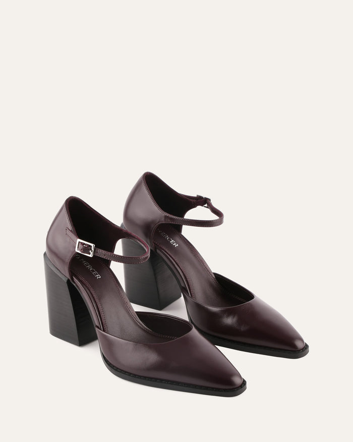 Pair of dark brown high-heeled shoes with a strap on a light gray background