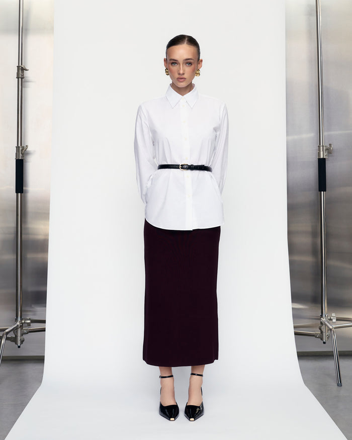 Person wearing a white shirt and black skirt standing against a plain background