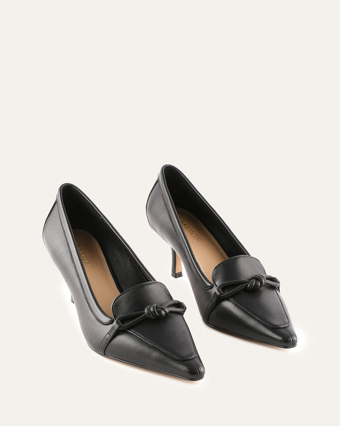 Pair of black high-heeled shoes with a bow detail on a light gray background