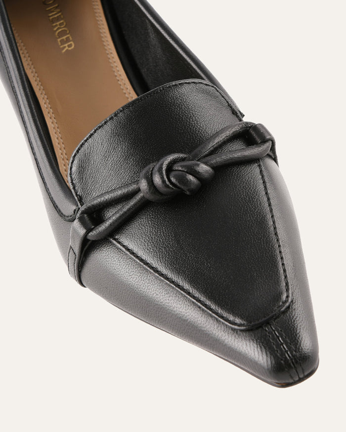 Black loafer shoe with a knot detail on a white background