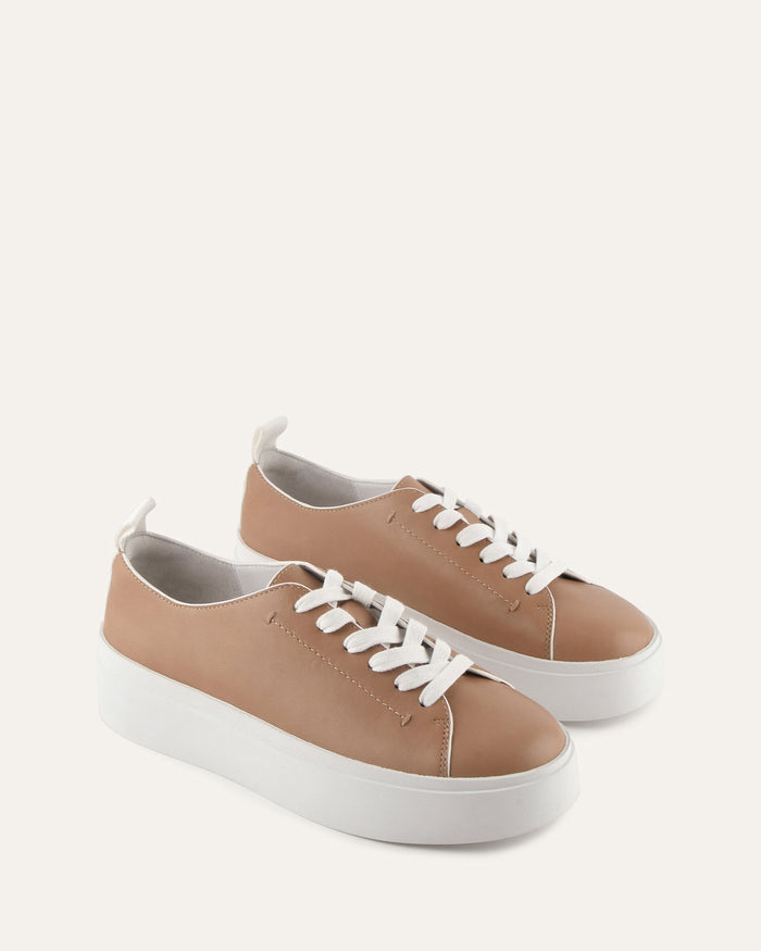 Pair of tan sneakers with white laces on a light beige background