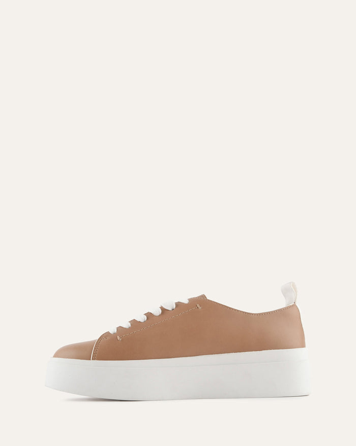 Tan sneaker with white sole on a light beige background