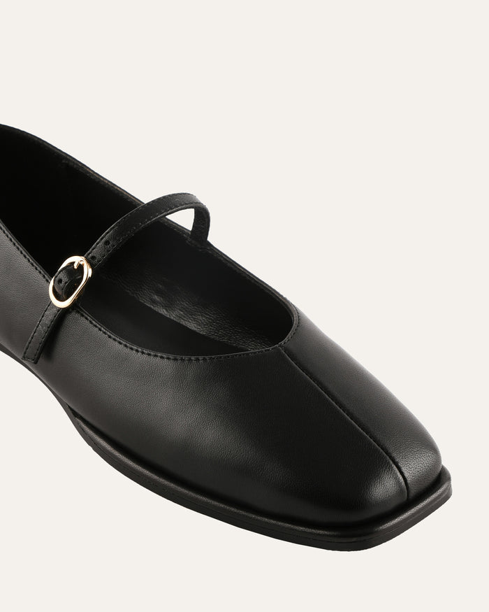 Black leather flat shoe with a strap on a light gray background