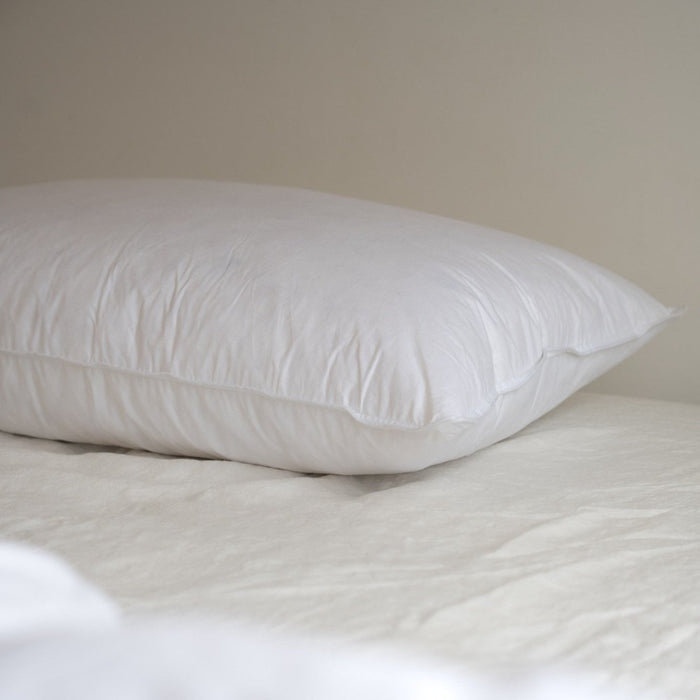 A close up of a white Somn Home luxury duck feather pillow insert cushion insert on a bed.