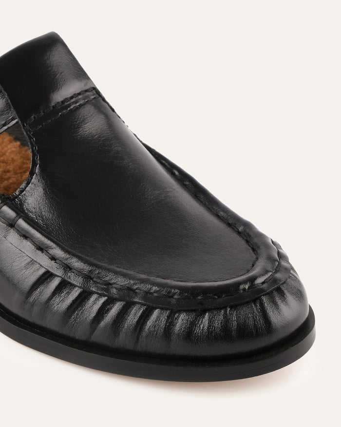 Black leather loafer shoe on a light gray background