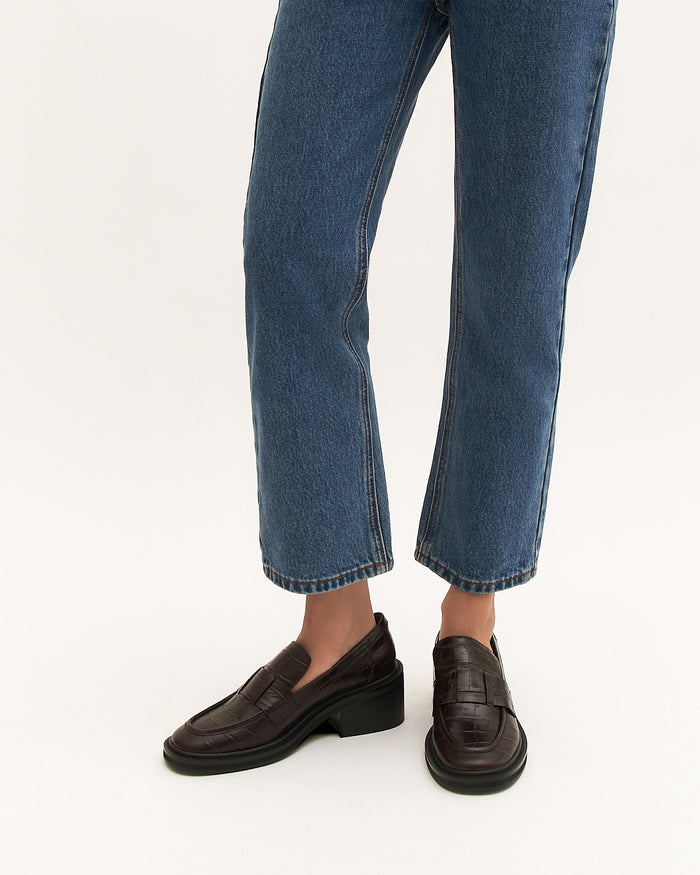 Person wearing blue jeans and brown loafers on a white background