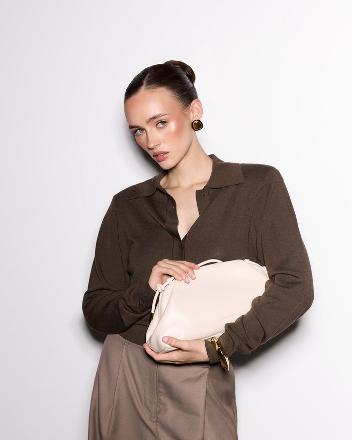 Woman holding a beige clutch against a plain background