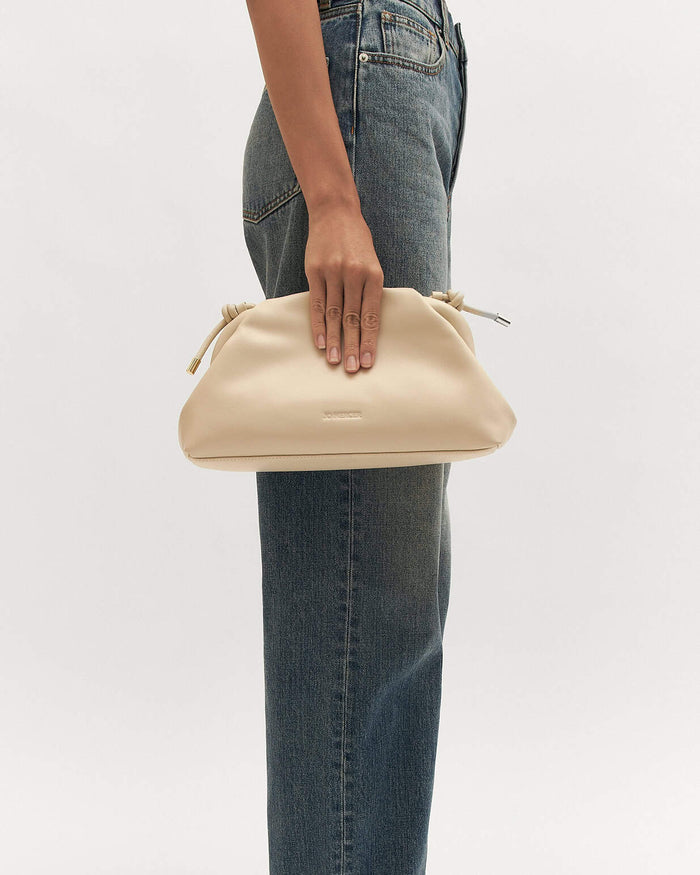 Beige handbag held by a person wearing blue jeans on a white background
