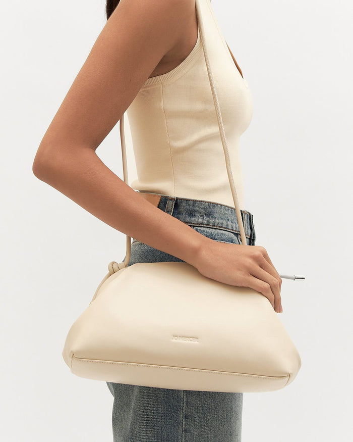 Person holding a cream-colored handbag against a plain background