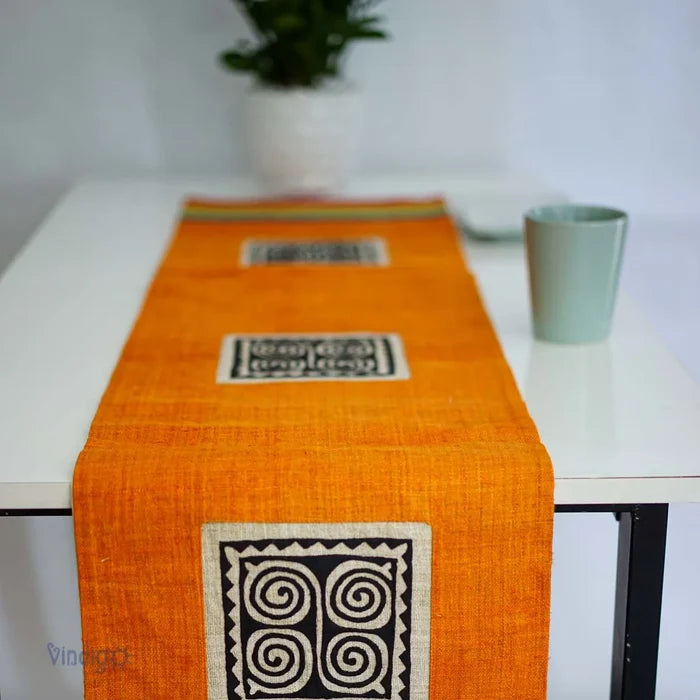 Bordslöpare i orange hampa med tribalruta dukad på vitt bord
