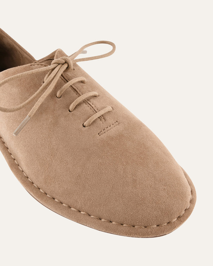 Beige suede shoe with laces on a light beige background