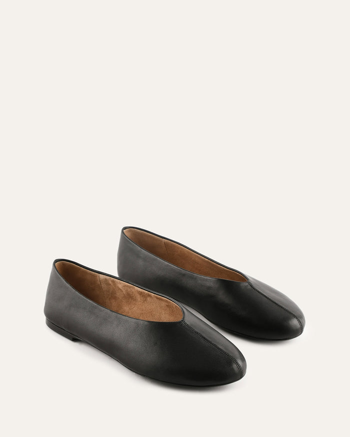 Pair of black leather flats on a light beige background