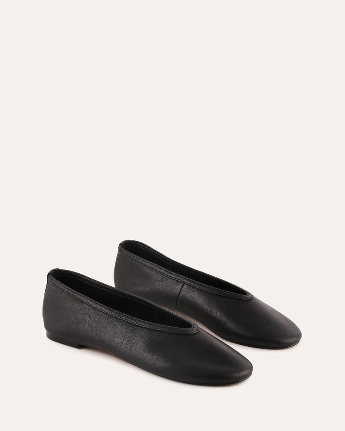 Pair of black leather flats on a light beige background