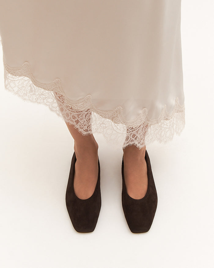 Black shoes worn with a white lace-trimmed skirt on a white background