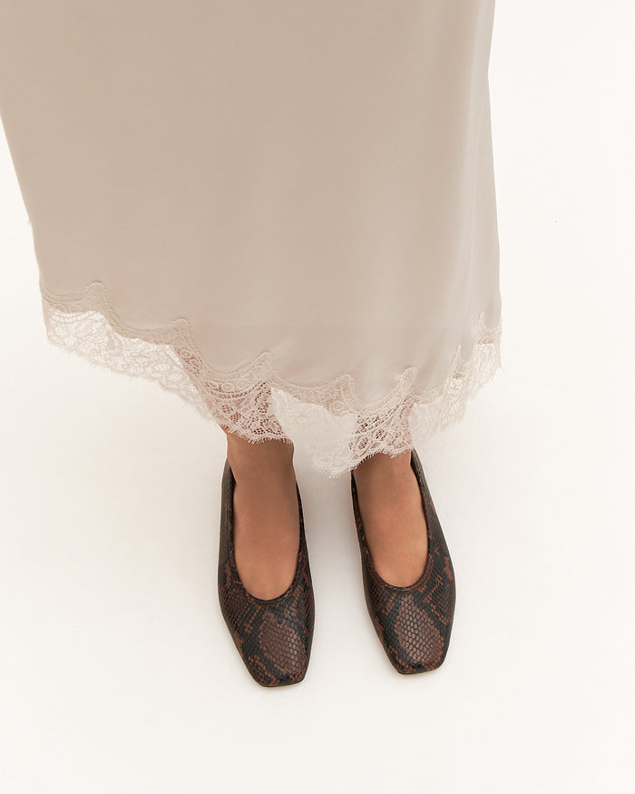 Black patterned flats worn with a white skirt on a white background