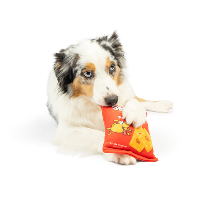 Dog holding an orange Sneeze-It plush toy featuring Sneeze-It (Double Sided).
