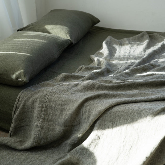 Bed with green bedding and pillows in a softly lit room.