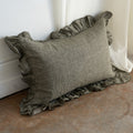 Green pillow with ruffled edges on a textured surface next to white curtains.