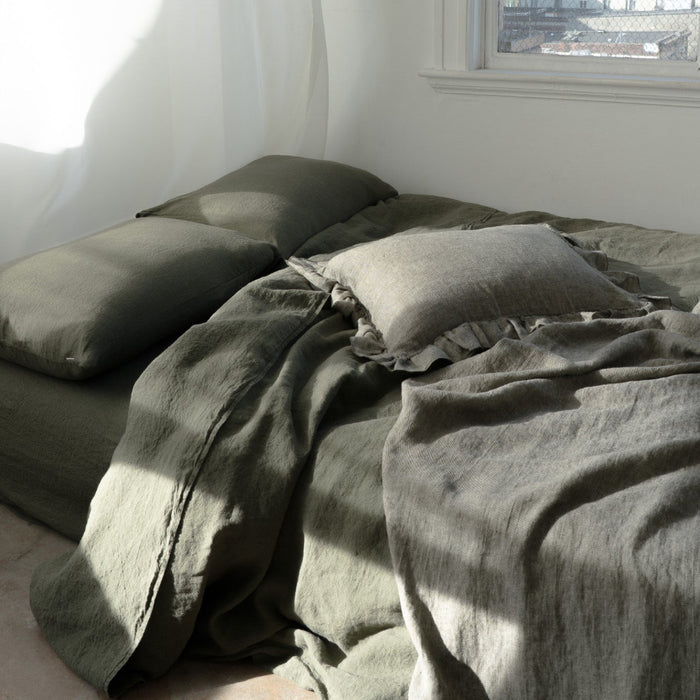 Bed with green bedding in a bright room with large windows.