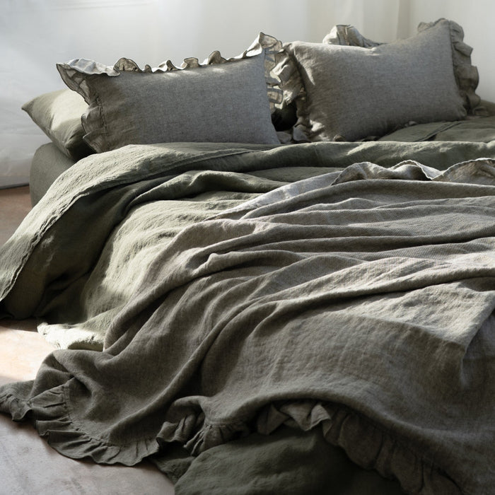 Bed with olive green bedding and pillows in a softly lit room.