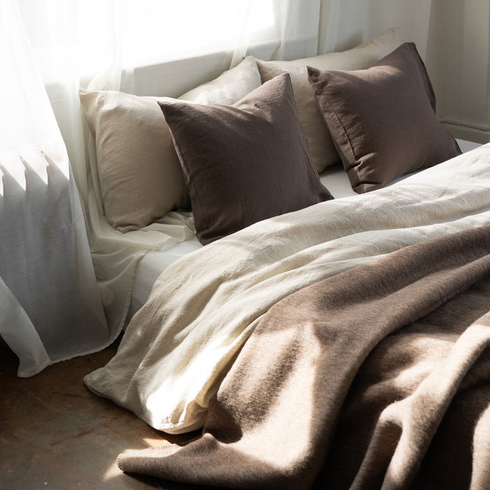 Cozy bedroom with pillows and a blanket on a bed, soft natural light filtering through curtains.