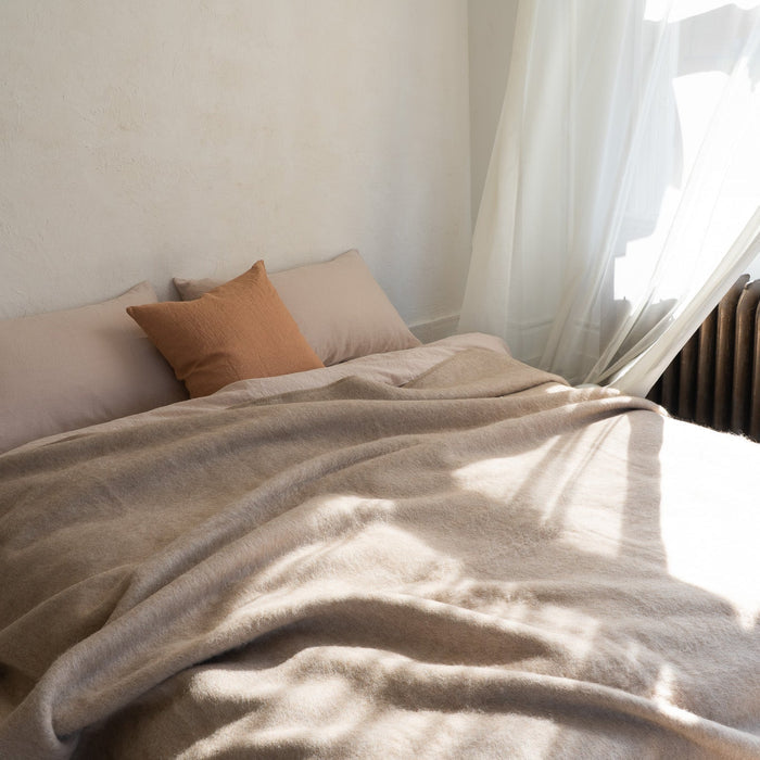 Neatly made bed with beige blanket and pillows in a softly lit room.