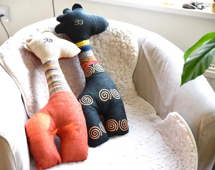 Two handmade deer plushies in orange and blue snuggled on sofa